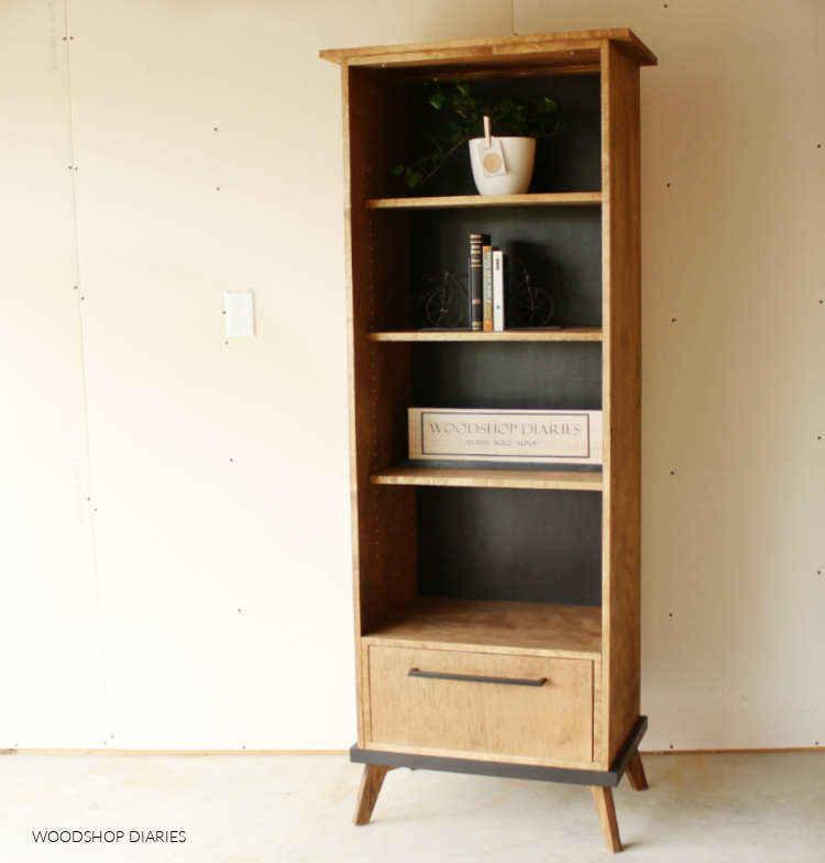 Black and wood mid century modern DIY bookcase cabinet with adjustable shelves and drawer against plan white wall