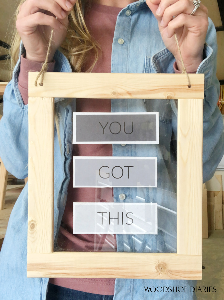 Shara Woodshop Diaries holding floating picture frame up showing "you got this" in the middle