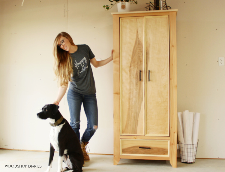 Shara Woodshop Diaries with shop dog Lucy standing next to Finished plywood and 2x4 DIY armoire wardrobe cabinet in garage