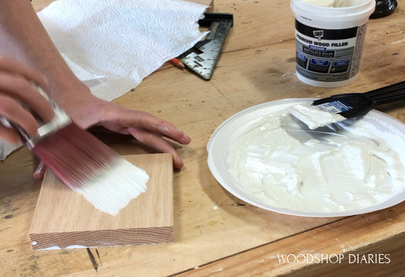 using paint brush to apply wood grain filler against the grain on scrap red oak block