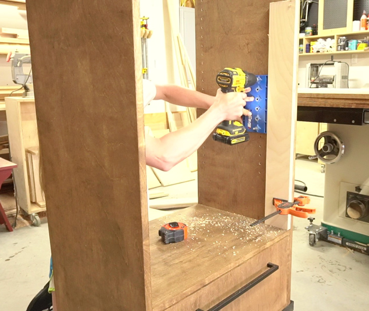 Shara drilling shelf pin holes into cabinet sides