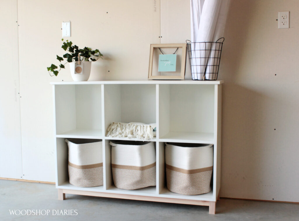 White and wood six cubby DIY shelf made with plywood and 2x2s.  Three khaki baskets are in the shelf cubbies