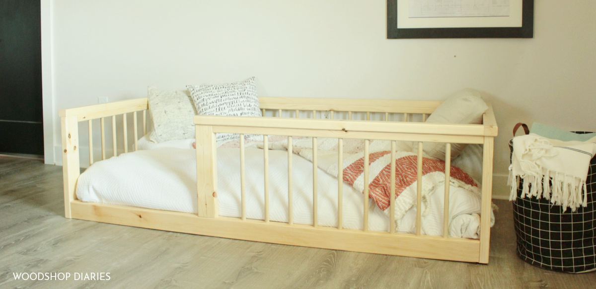 Finished DIY toddler bed frame sitting on floor with white bedding