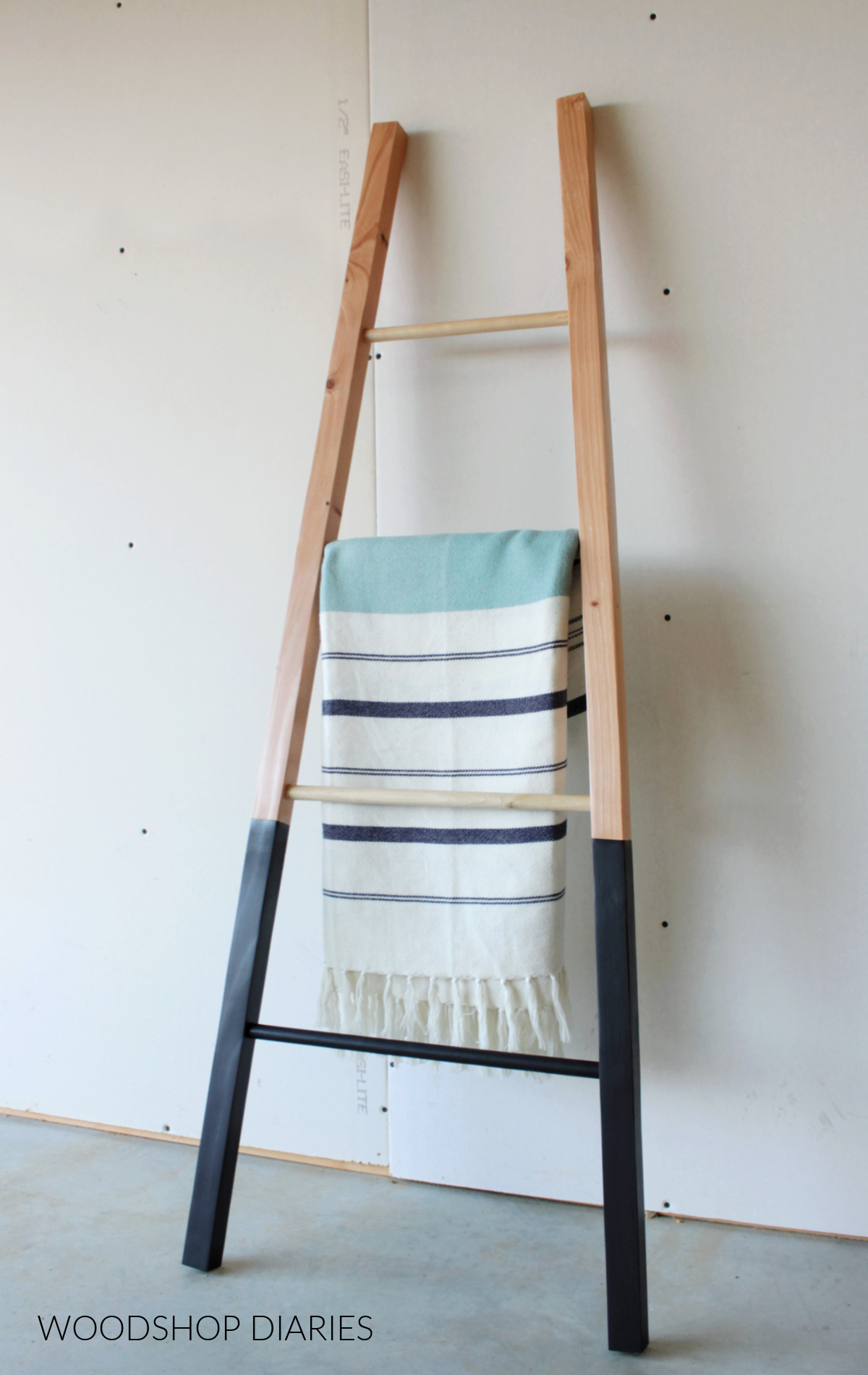 DIY wooden black and wood blanket ladder leaning against the wall with white and navy blanket hanging on it