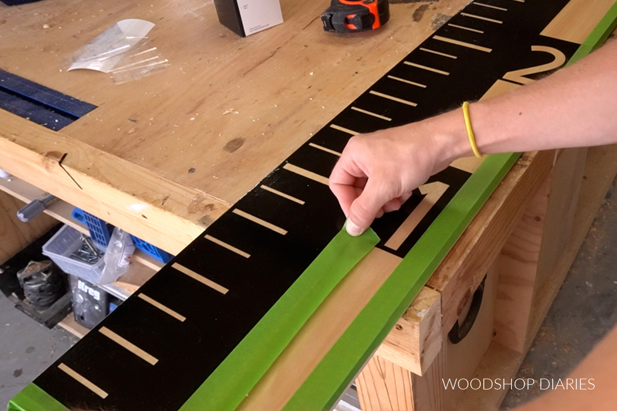 Applying painters tape to exposed wood before spray painting giant life size ruler board