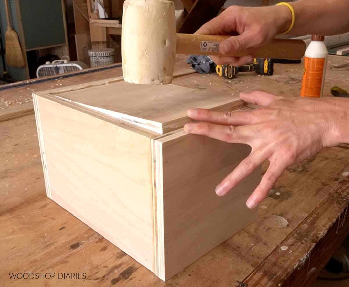 Using rubber mallet to tap bottom panel of scrap wood keepsake box in place