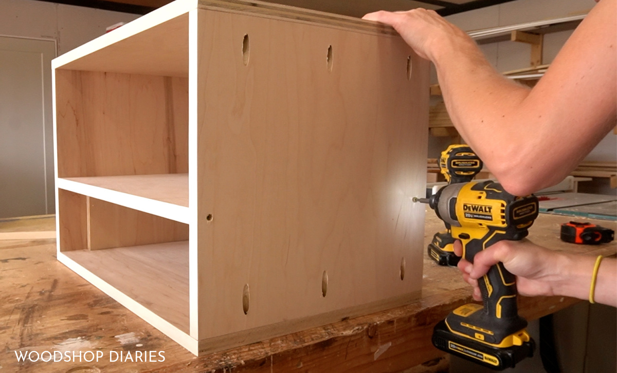 Shara Woodshop Diaries driving screws through side panels to attach shelf in place