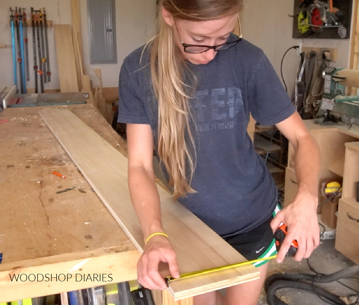 Shara Woodshop Diaries measuring giant ruler board width on workbench
