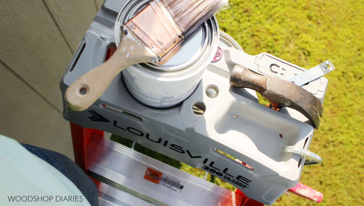 Close up of top section of Louisville step ladder with paint can, hammer, caulk gun clipped on