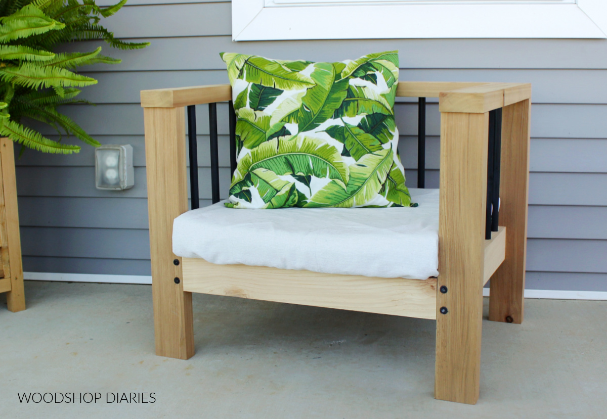 Simple modern DIY outdoor chair made from cedar and wood dowels sitting on front porch with cushion and pillow