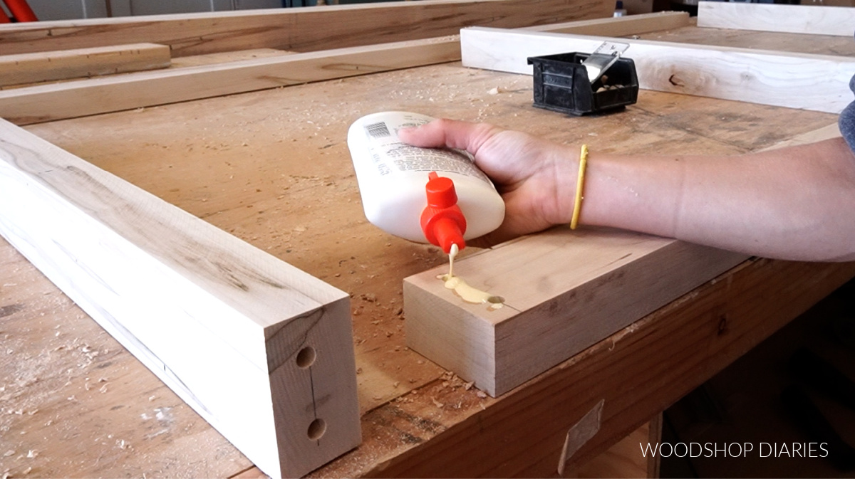 Applying wood glue to dowel holes to assemble dining table apron