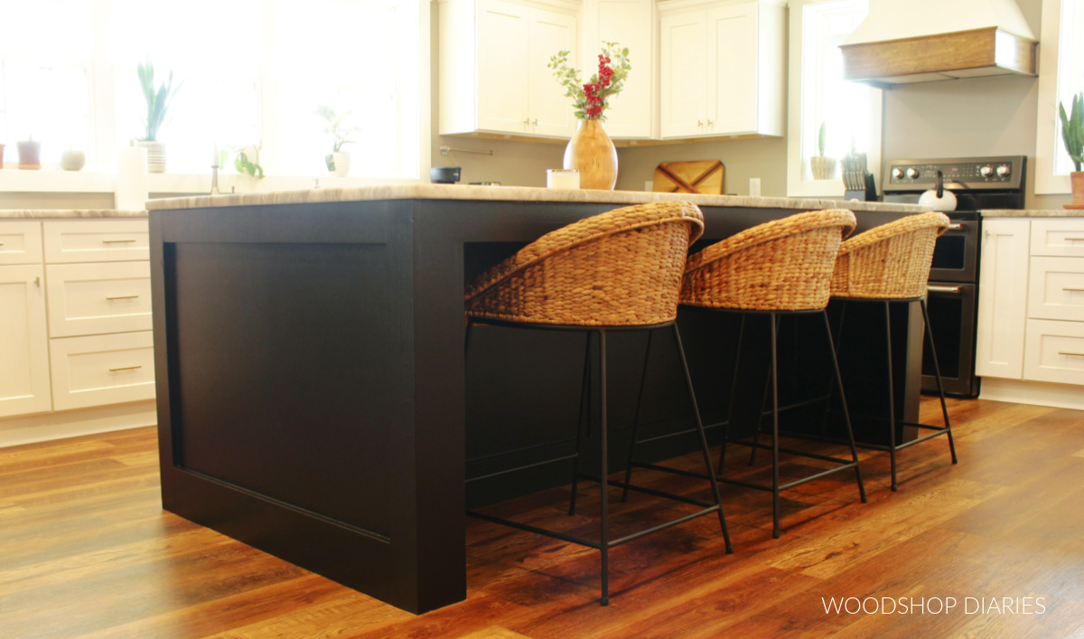 White kitchen cabinets with black island and wicker bar stools
