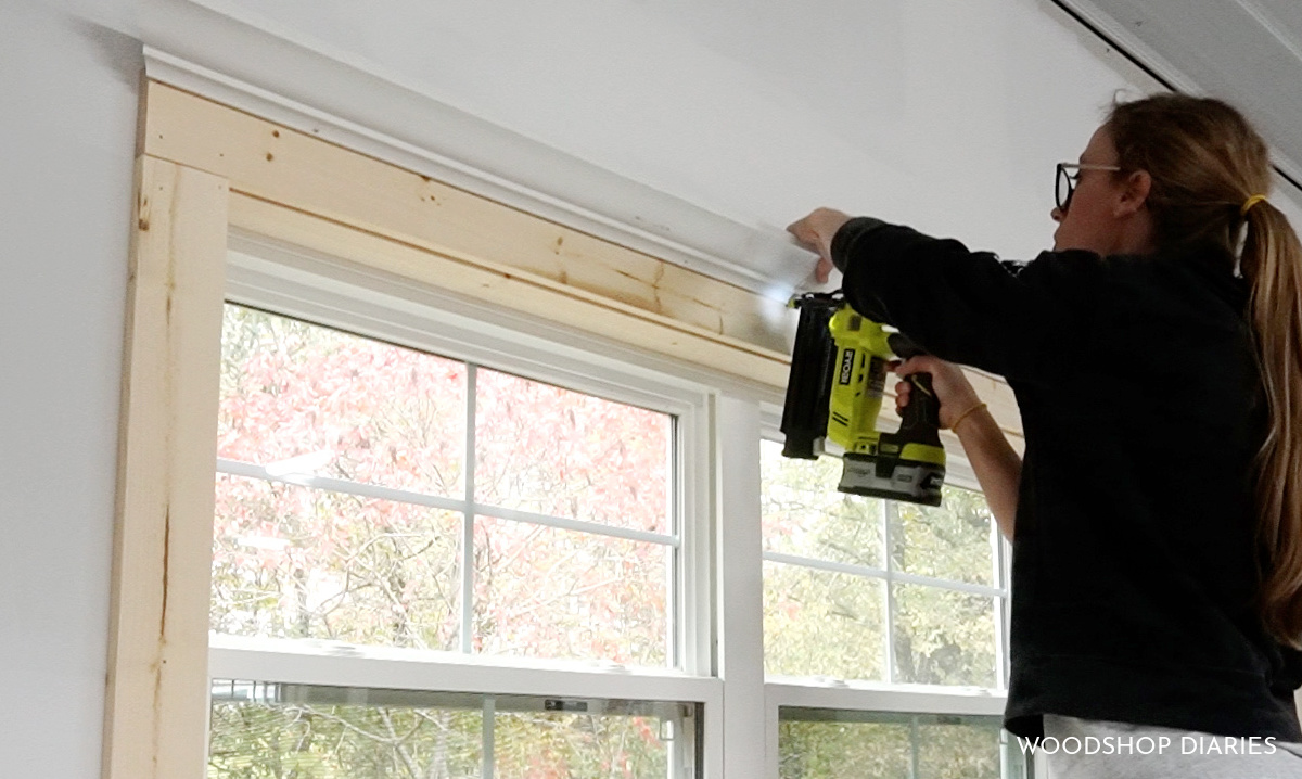 Shara Woodshop Diaries using 18 gauge nail gun to secure crown molding along window trim in workshop