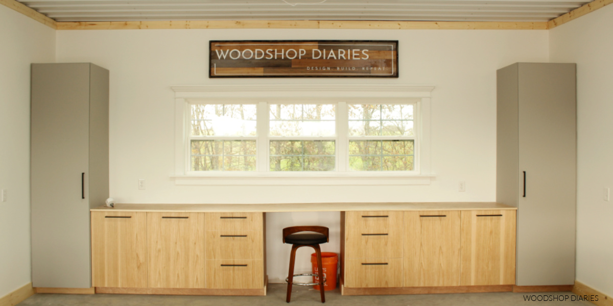 Woodshop Diaries back wall with cabinets, large window, and large wooden sign hanging at top in center