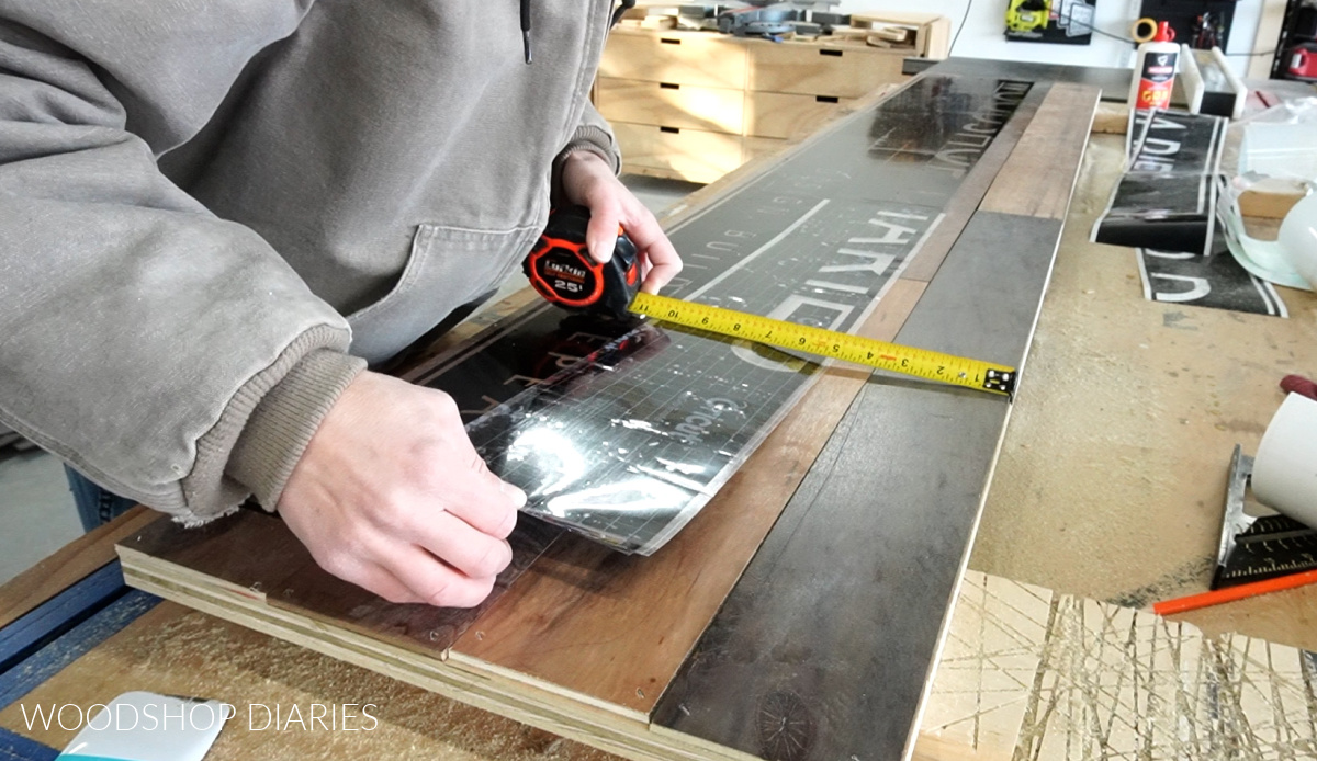 Applying vinyl stencil in pieces onto top of large wooden sign planks