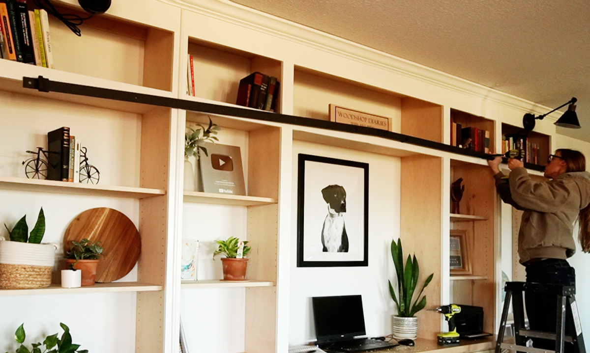 Shara Woodshop Diaries installing rolling library ladder track onto bookshelf