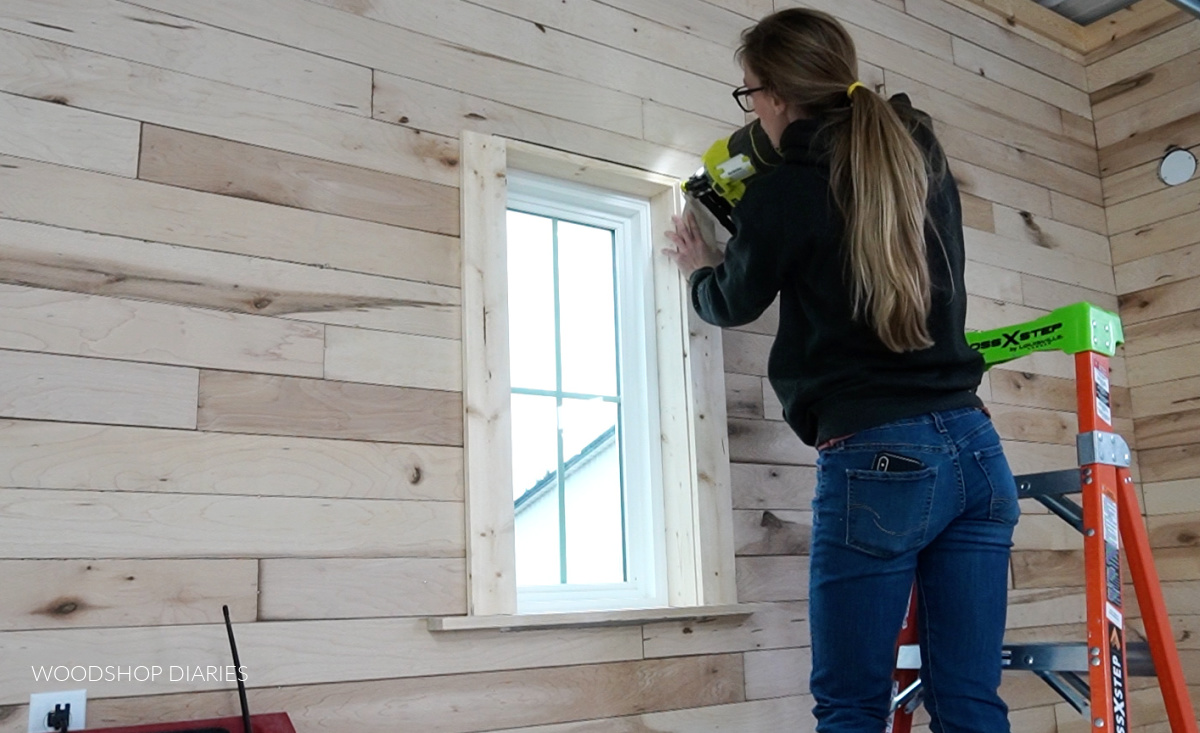 Shara nailing window trim around window in wood accent wall