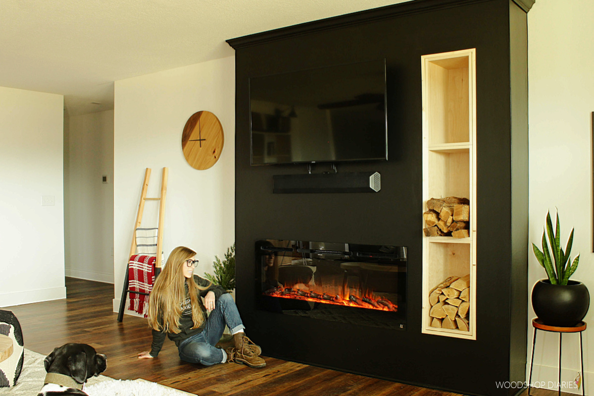 Shara Woodshop Diaries sitting next to fireplace on black feature wall in living room