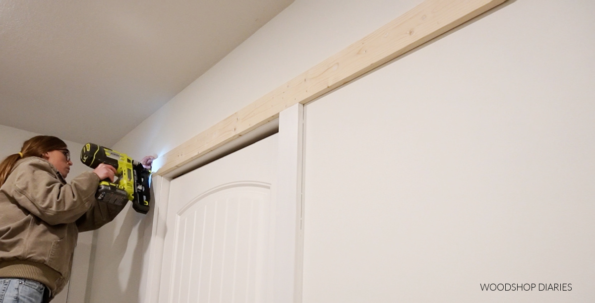 Shara Woodshop Diaries nailing new trim piece above laundry room door to install sliding door hardware rail