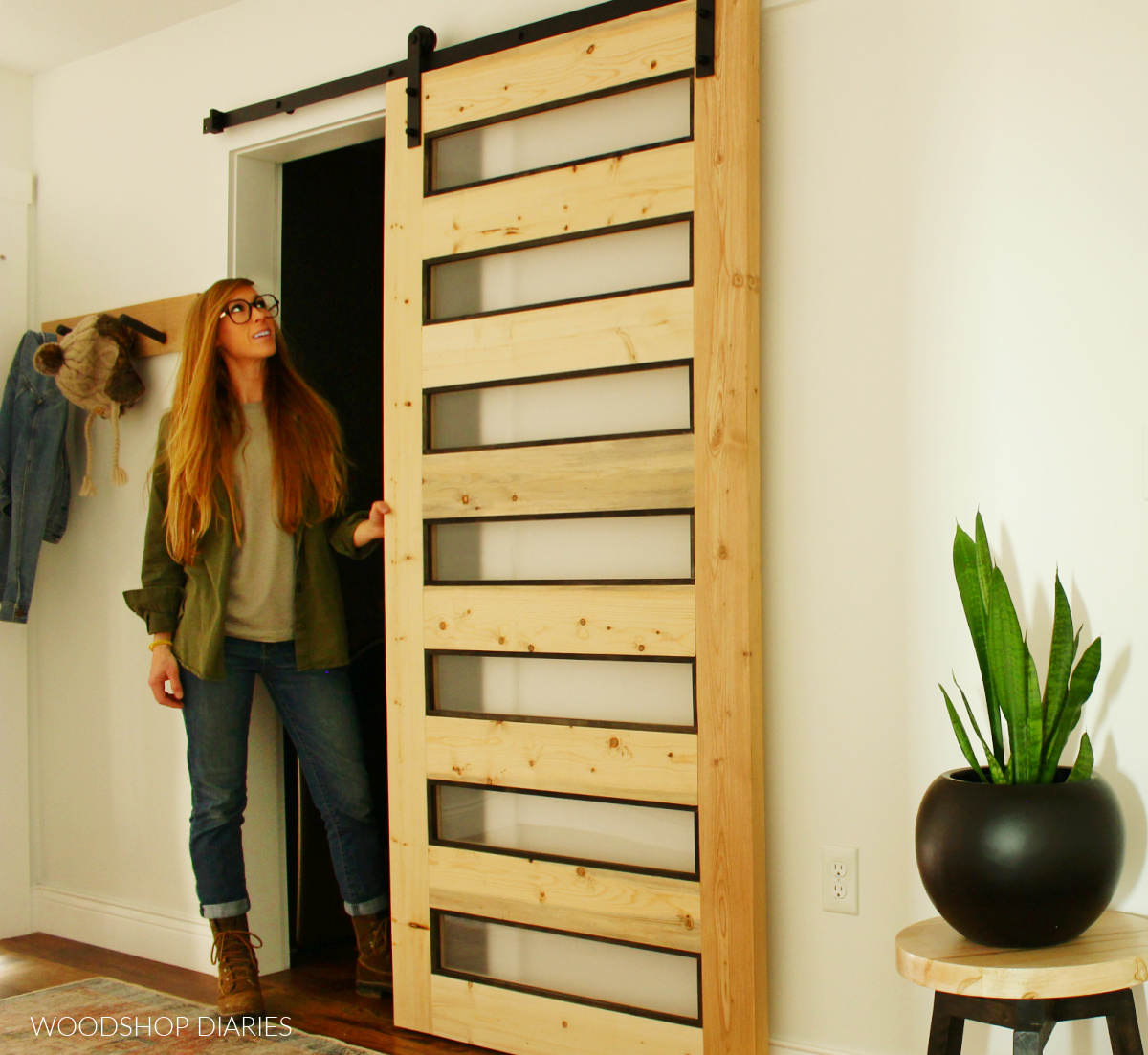 Shara Woodshop Diaries standing next to wood and black MODERN DIY sliding door in white hallway by laundry room