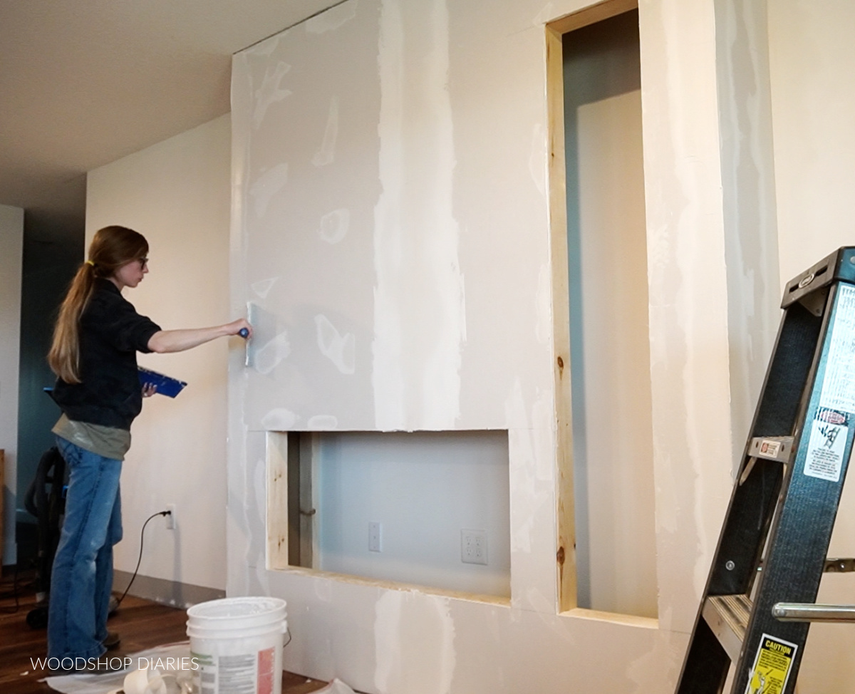 Shara Woodshop Diaries applying drywall mud to electric fireplace wall box