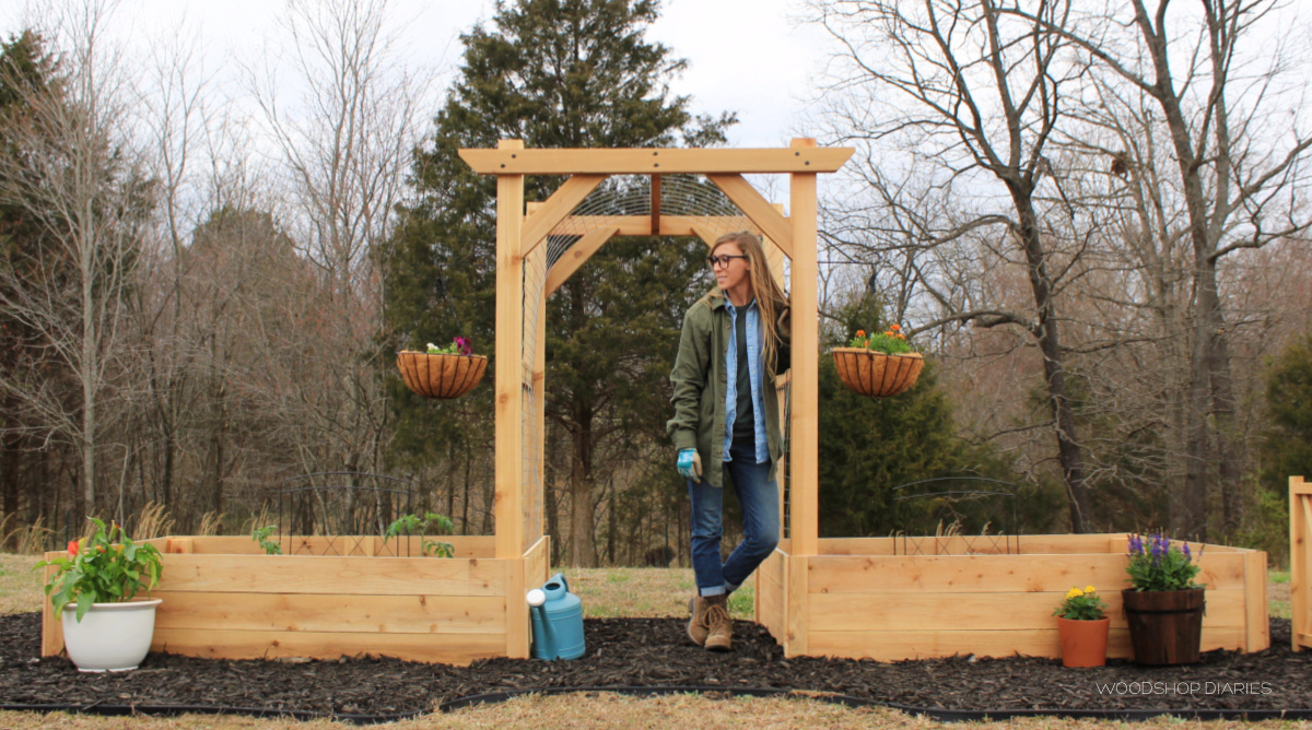 Shara standing in garden arbor between raised beds on mulch