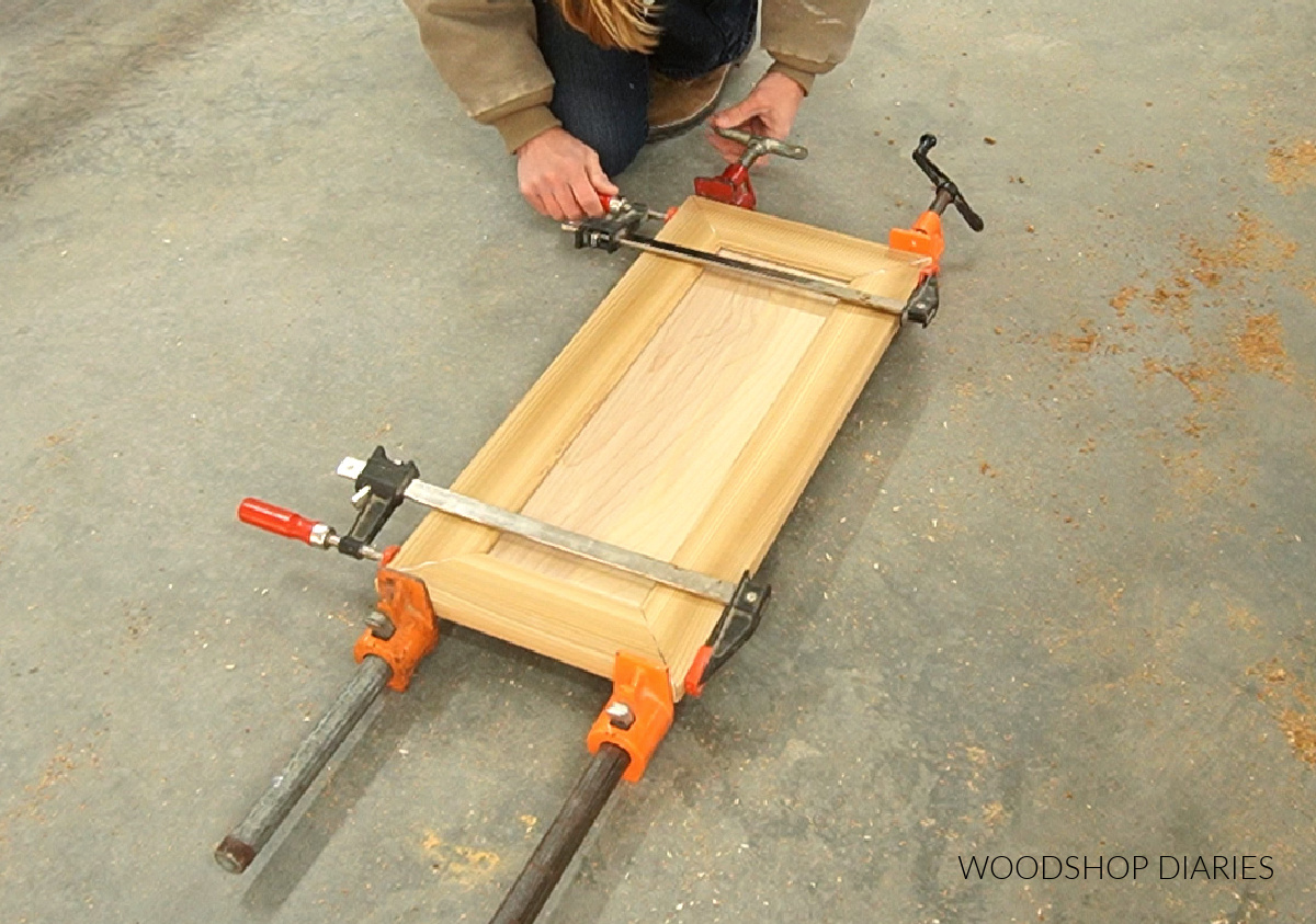 Shara Woodshop Diaries clamping mitered corner cabinet door together on workshop floor