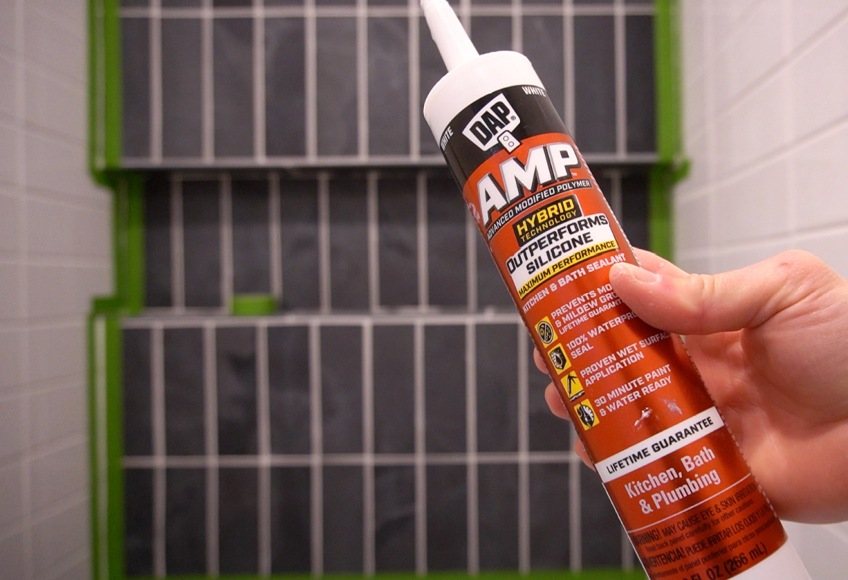 Close up of DAP AMP sealant tube in front of shower tiles