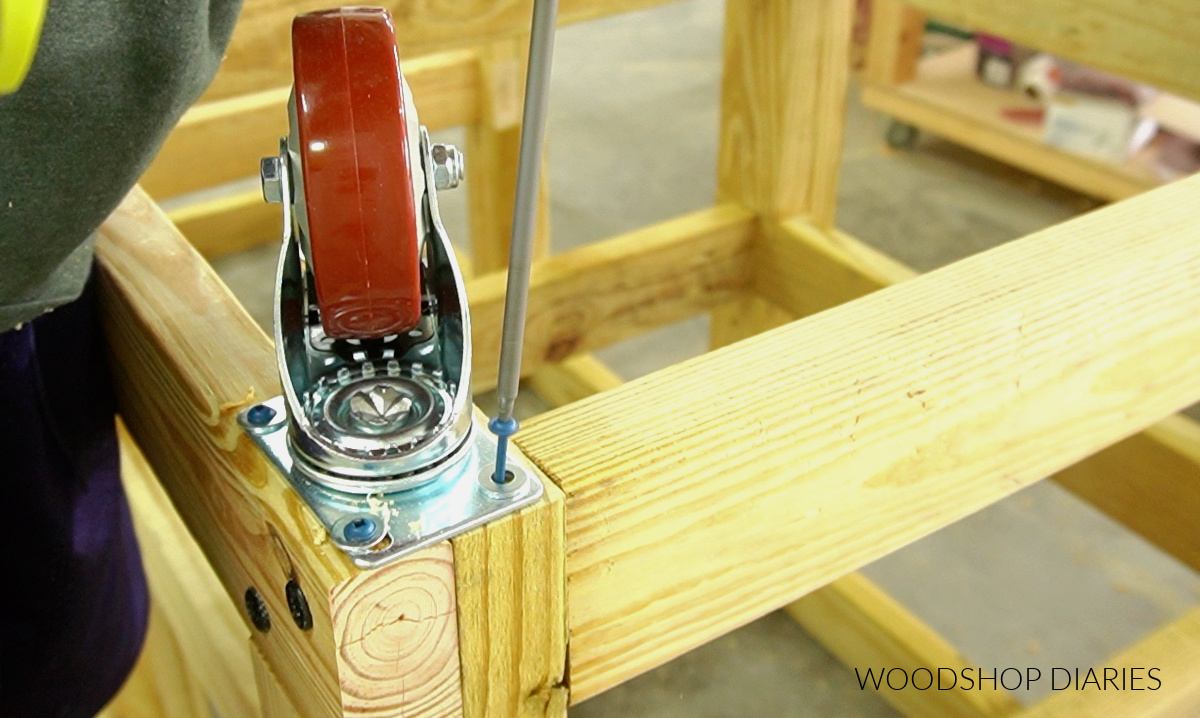 Close up of driving screws to install red heavy duty caster wheels on corner of grill cart frame