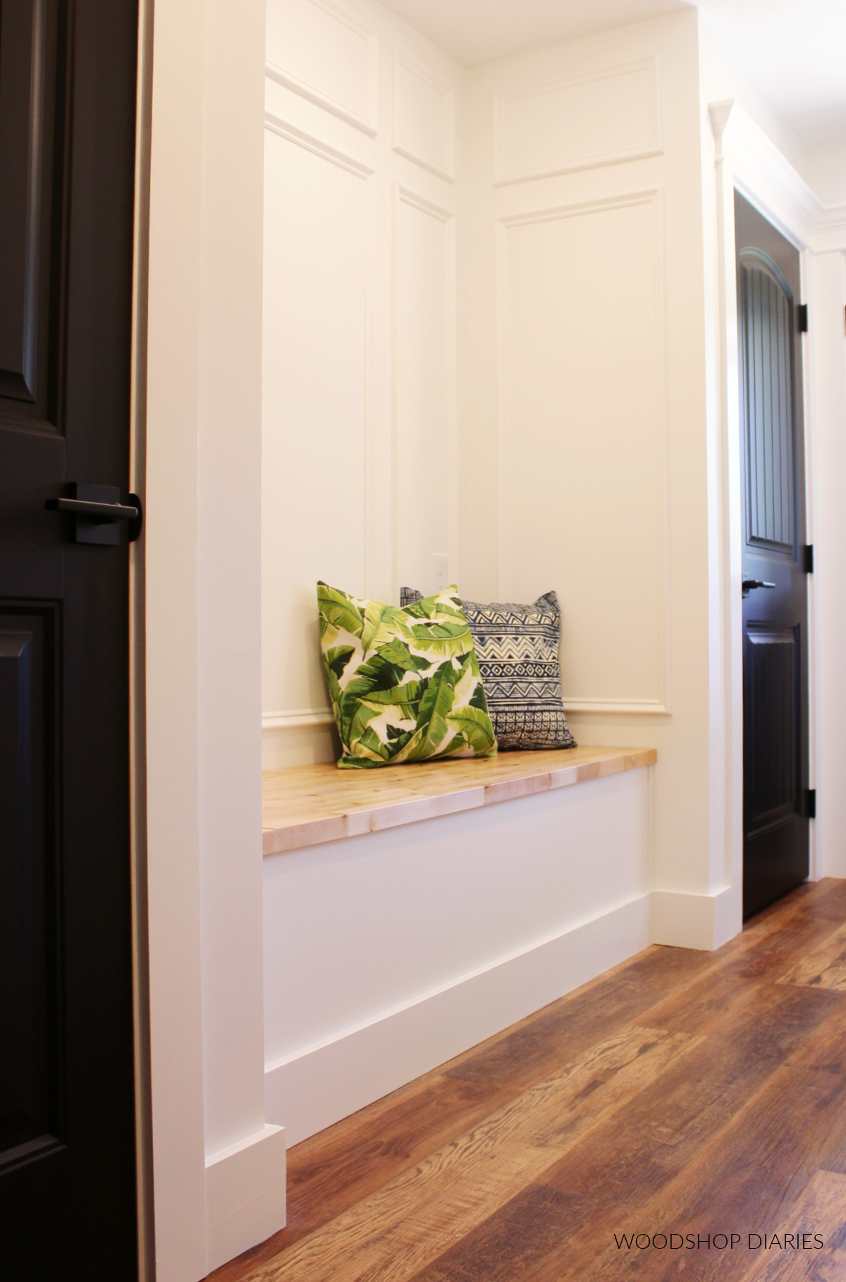 White walls with decorative base cap trim and built in bench with black doors and wooden bench seat