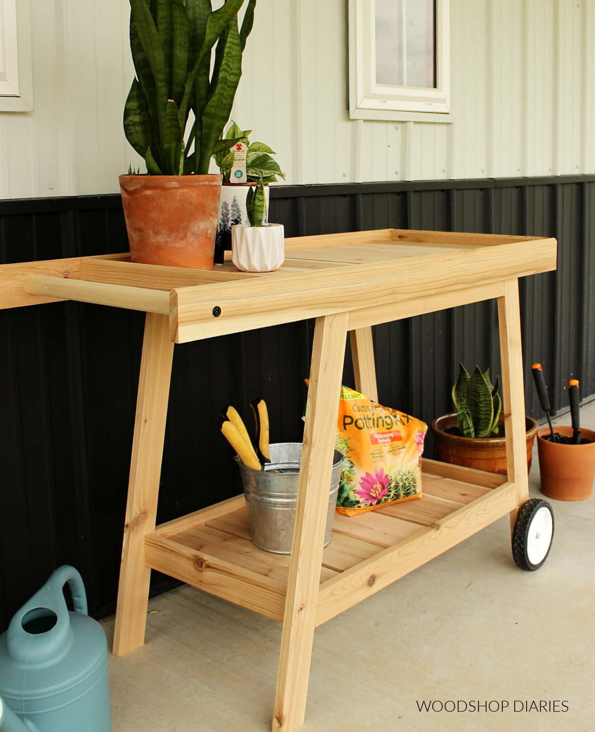 DIY Cedar potting bench with wheels against metal house with plants around it