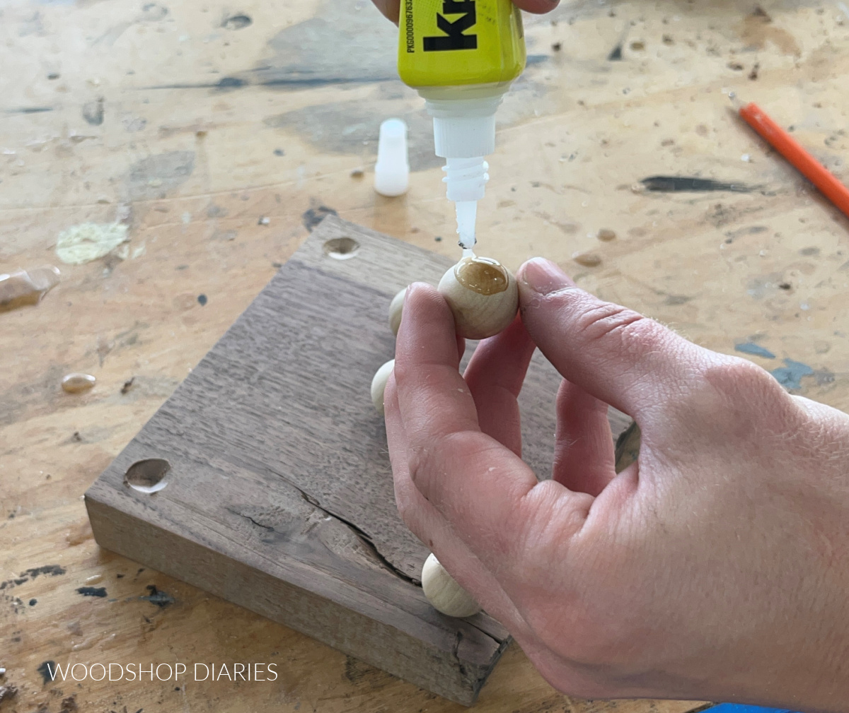 Close up of adding Krazy Glue Wood Glue to wooden balls to glue on board to make footed tray