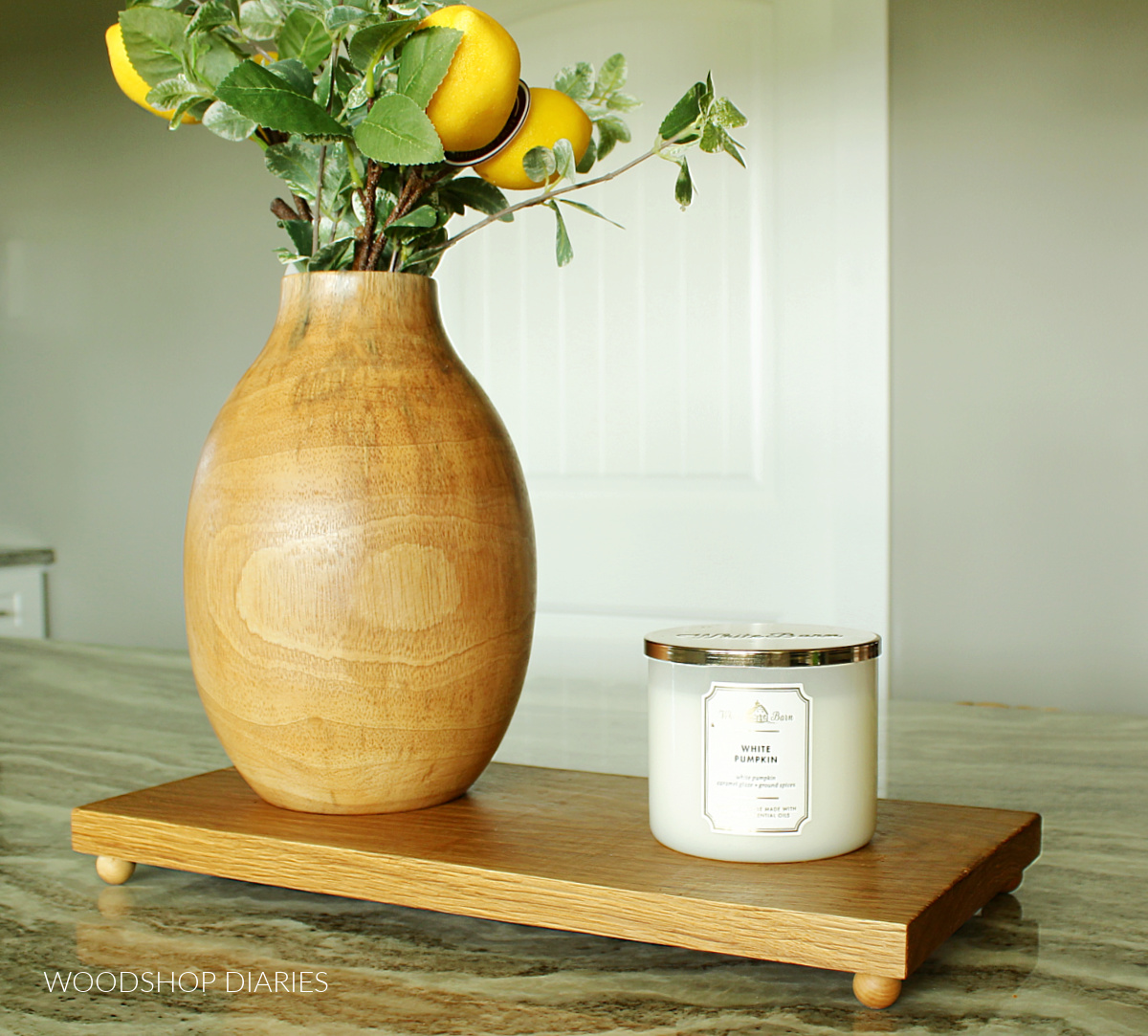 White oak wooden footed tray on granite countertop with wooden vase and candle on top