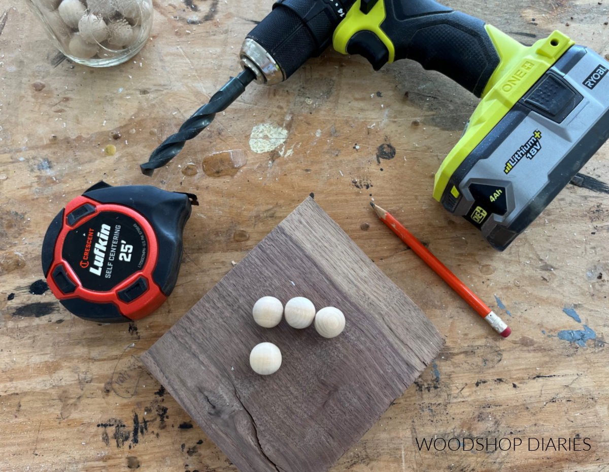 Measuring tape, scrap block, wooden balls, and drill laid out on workbench