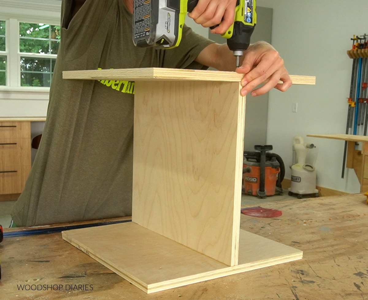 Driving screws into plywood pieces to assemble a capital "I" shape for charging station body