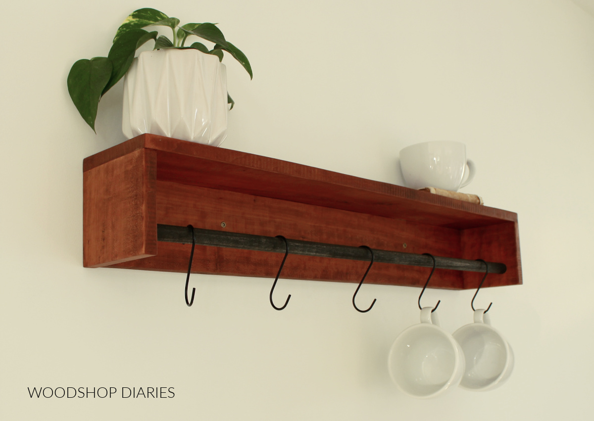 Close up of wall shelf flipped over and s hooks hanging coffee mugs from dowel