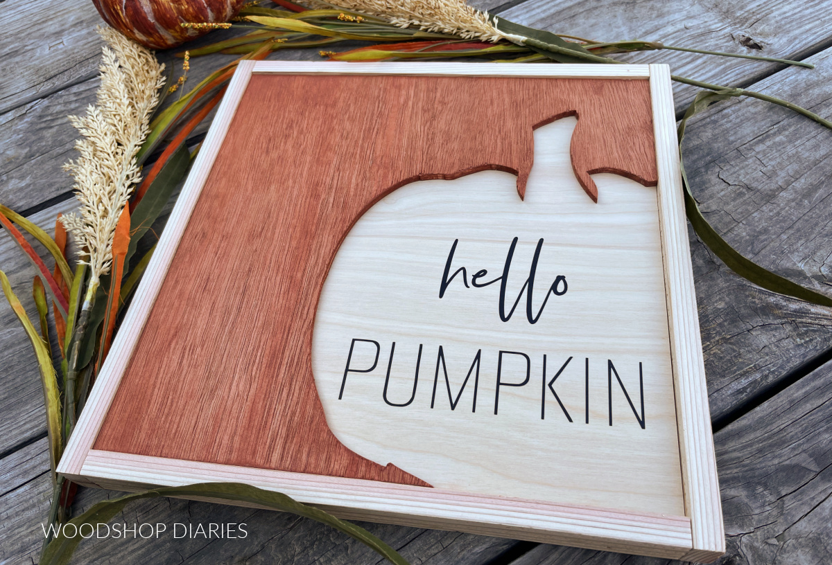completed hello pumpkin wood art sign on weathered wood back drop with fall foliage