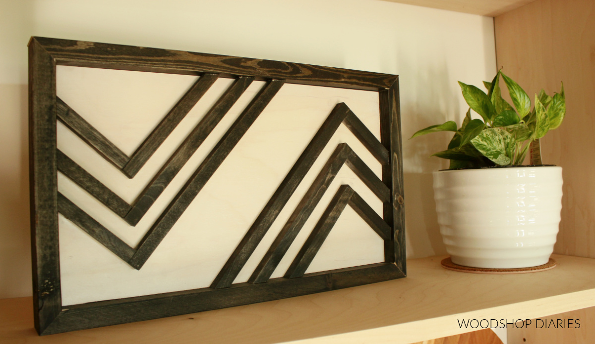 Black and white wooden art piece sitting on shelf next to plant