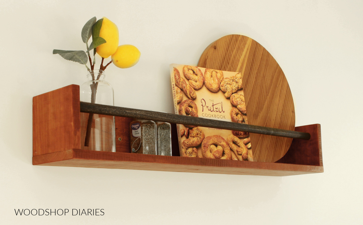 Wall shelf with dowel toward top with spices, book, and cutting board inside