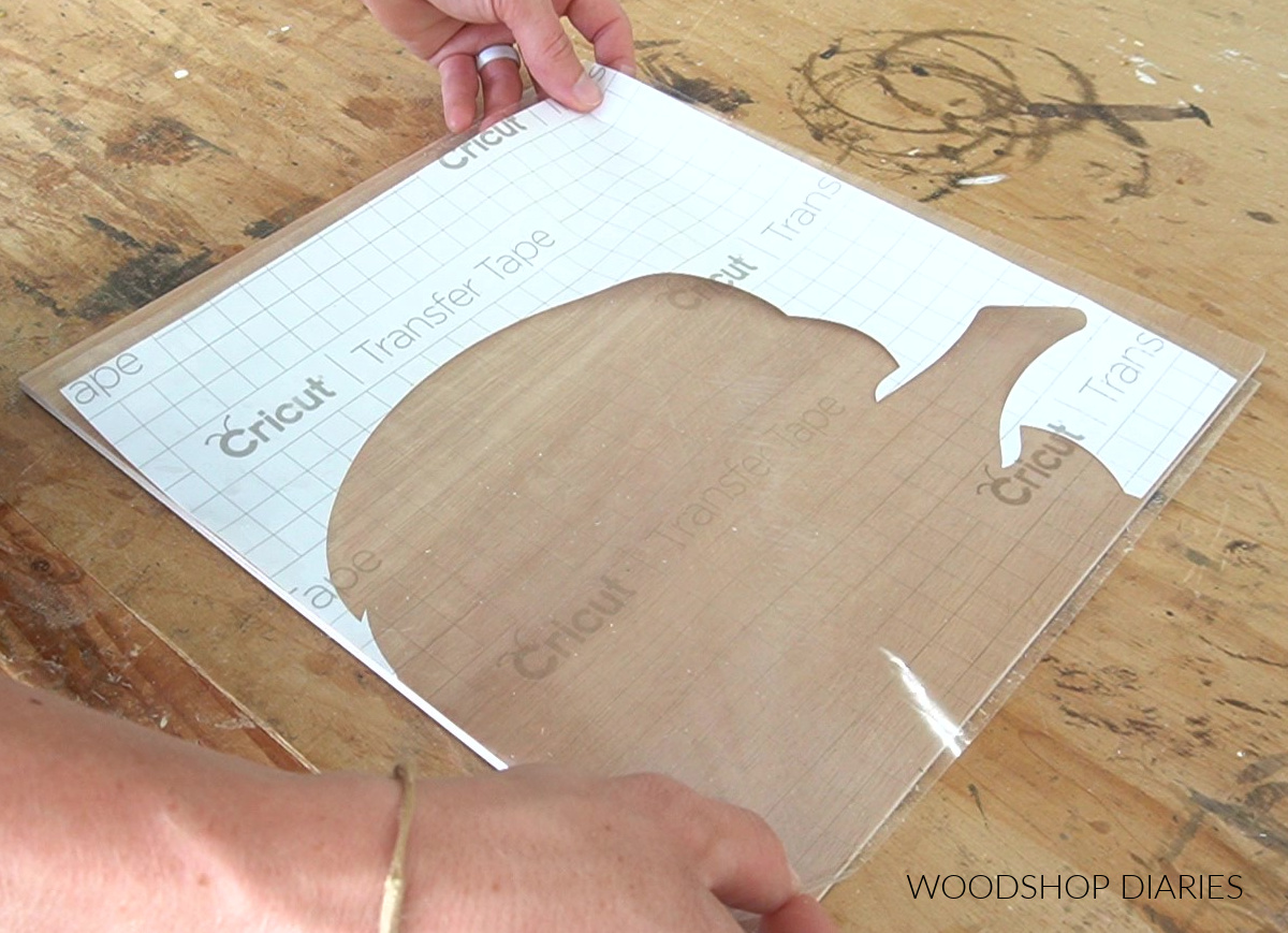 Placing pumpkin cut out shape vinyl stencil onto ¼" plywood piece