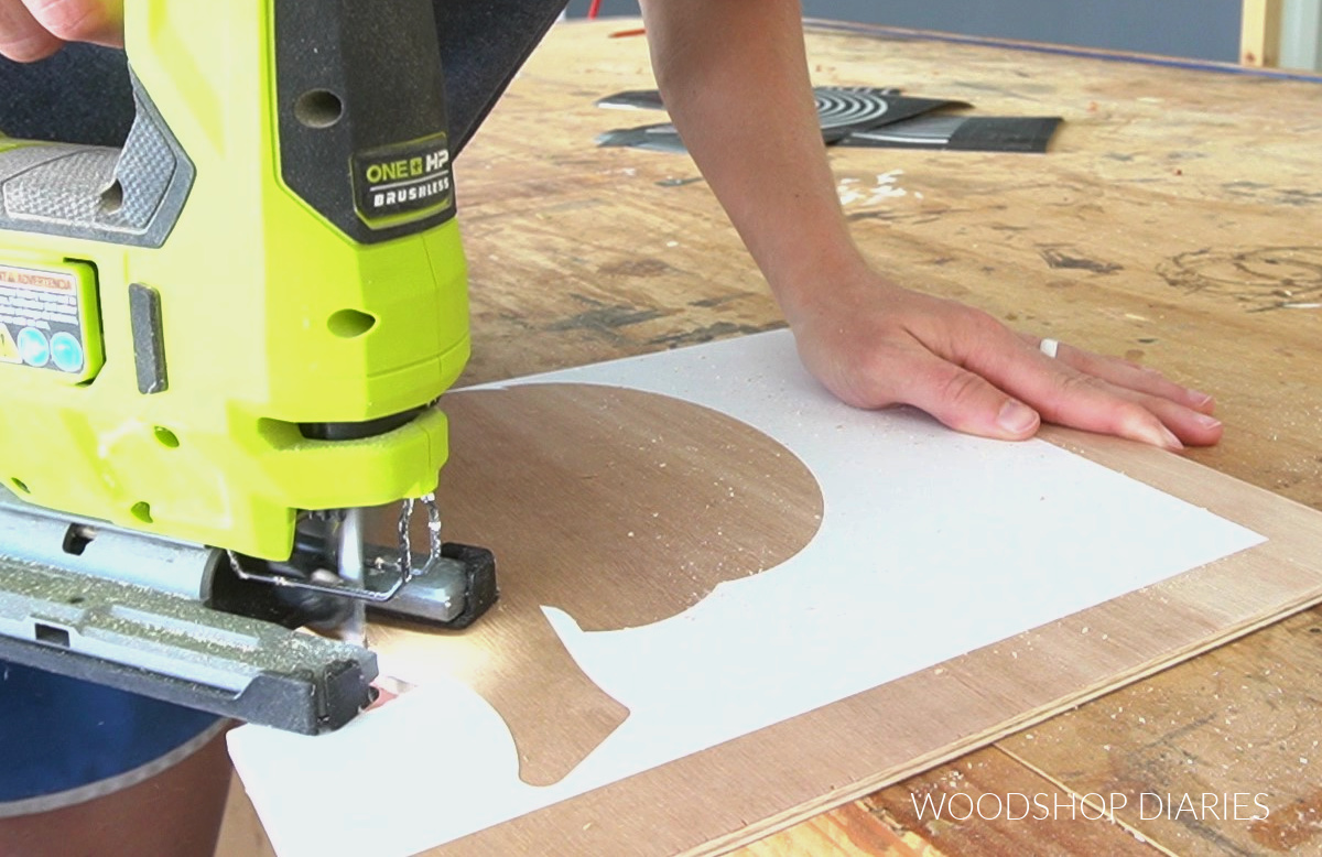 using a jig saw to cut around vinyl pumpkin stencil on plywood