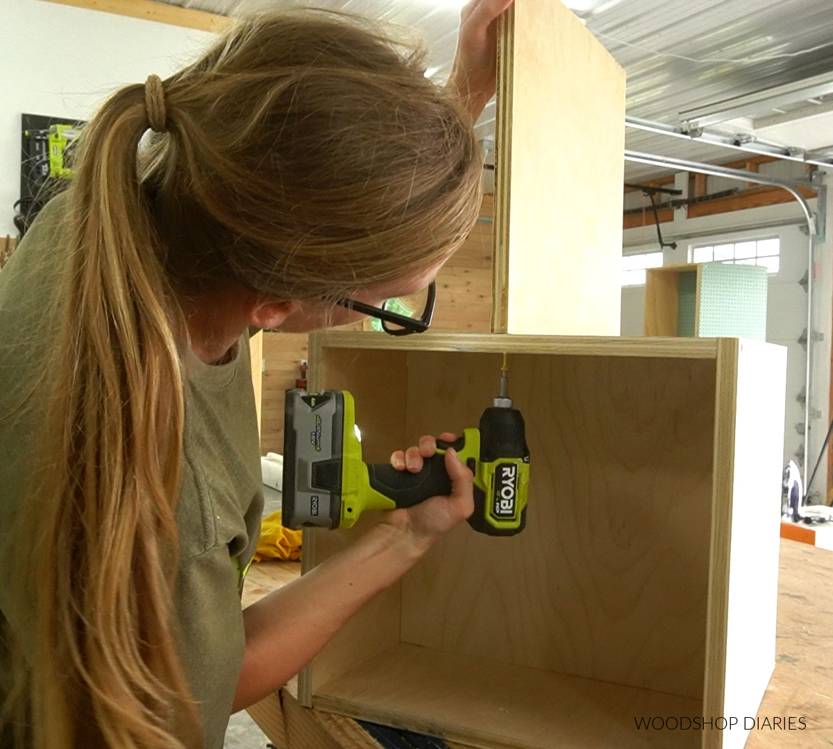 Shara Woodshop Diaries driving screws through plywood to attach top half of charging station box