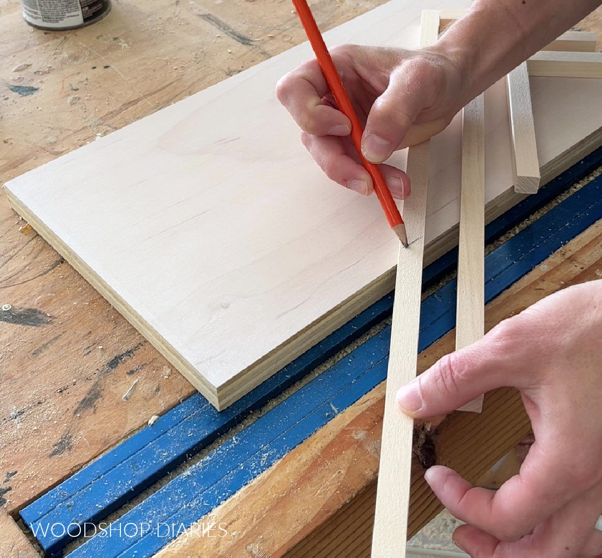 Using a pencil to mark length of square dowels on scrap wood art piece