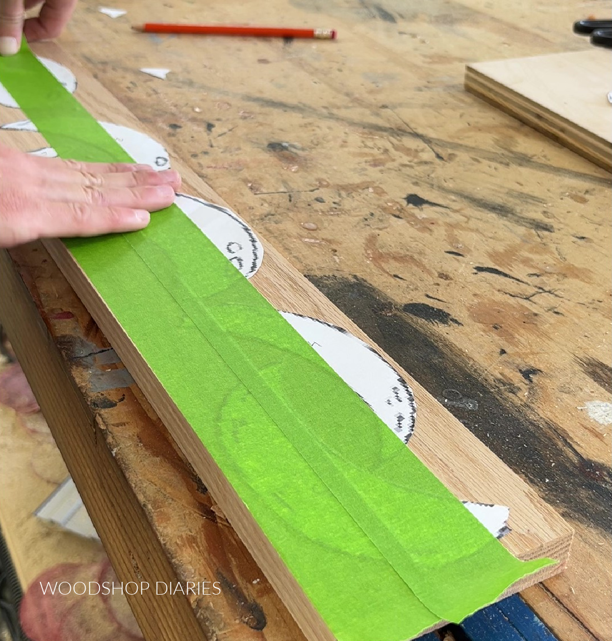 Shara Woodshop Diaries applying painters tape over paper cut outs laid out on red oak board