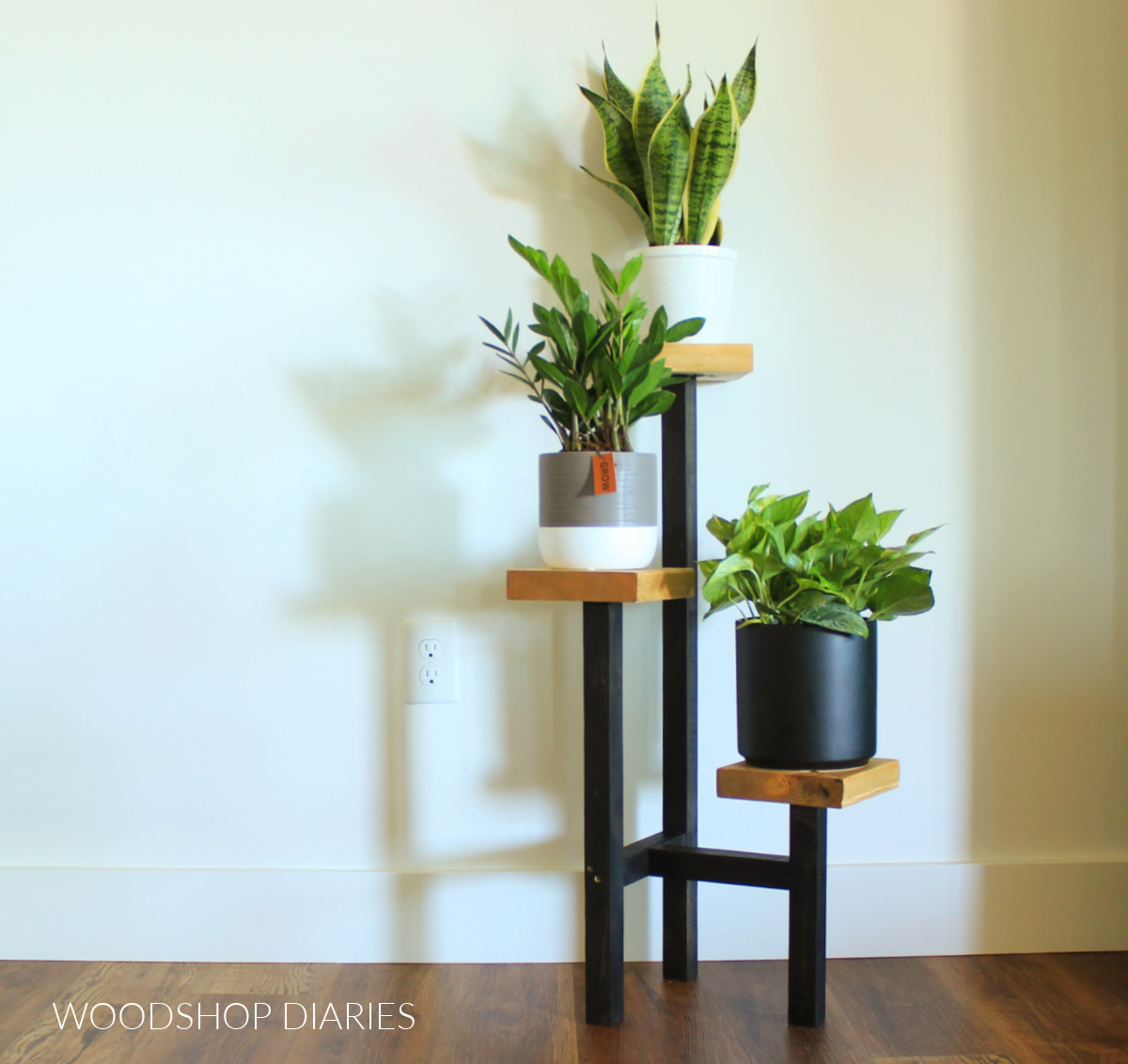 Completed plant stand black base and wood tops with three plants on each tier against white wall