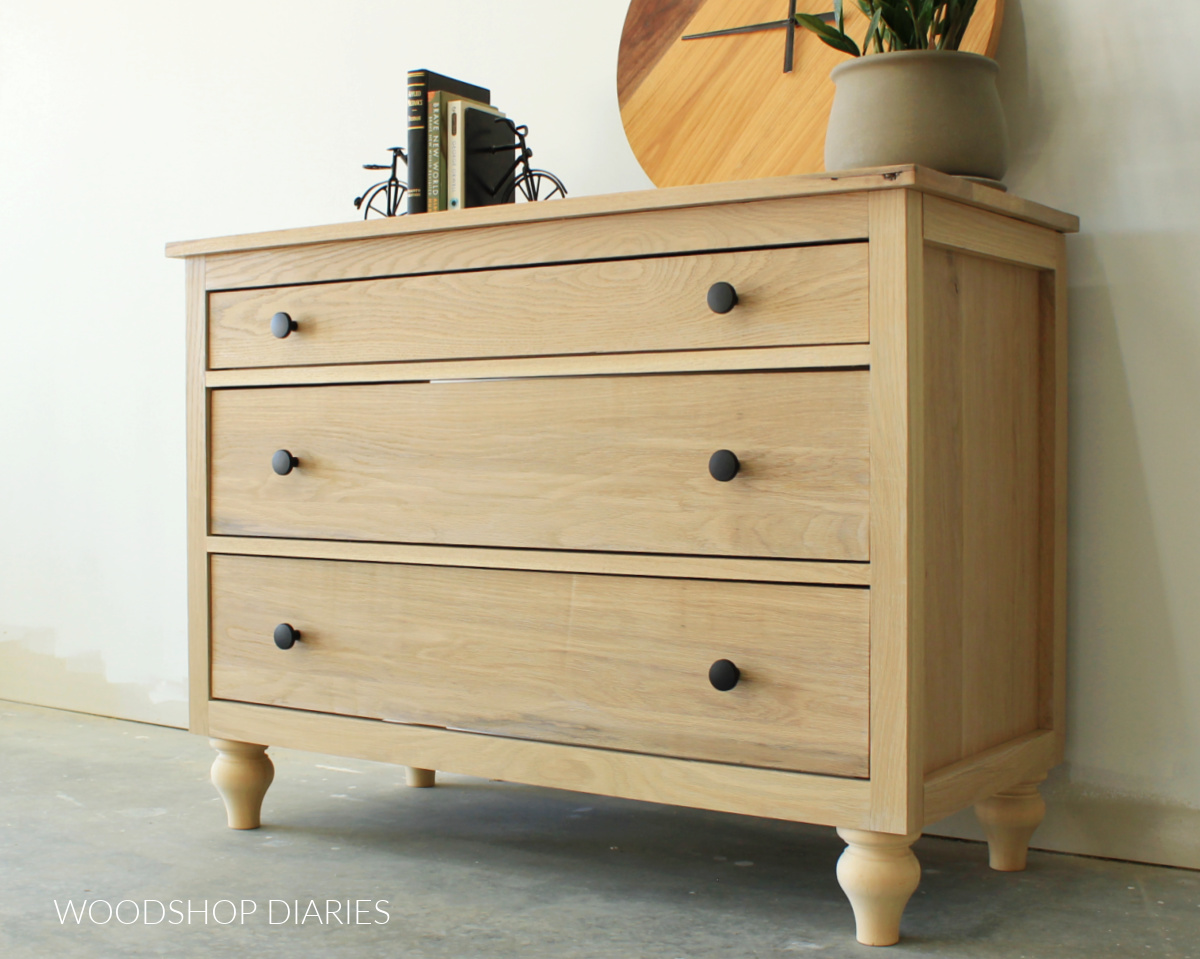 White oak 3 drawer dresser with decorative feet against white wall