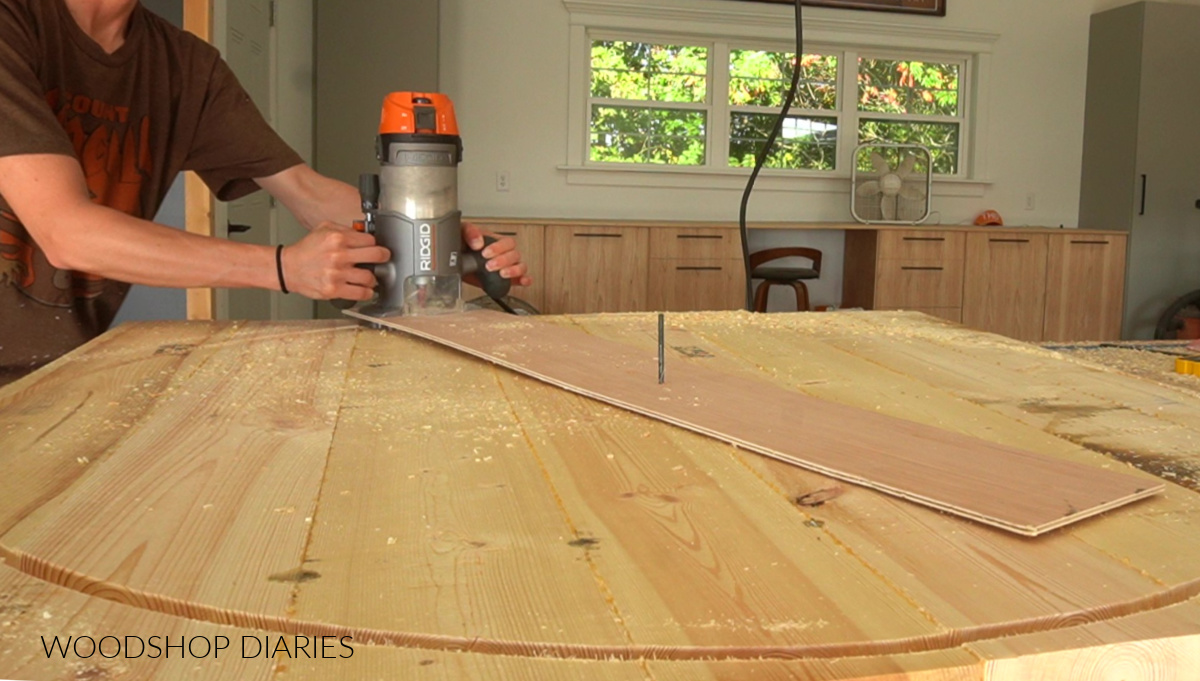 using a homemade circle jig with router to cut a wooden circle in large panel on workbench