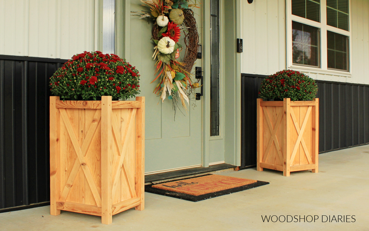 DIY wooden planter boxes with X trim on the sides on each side of front door with red mums inside