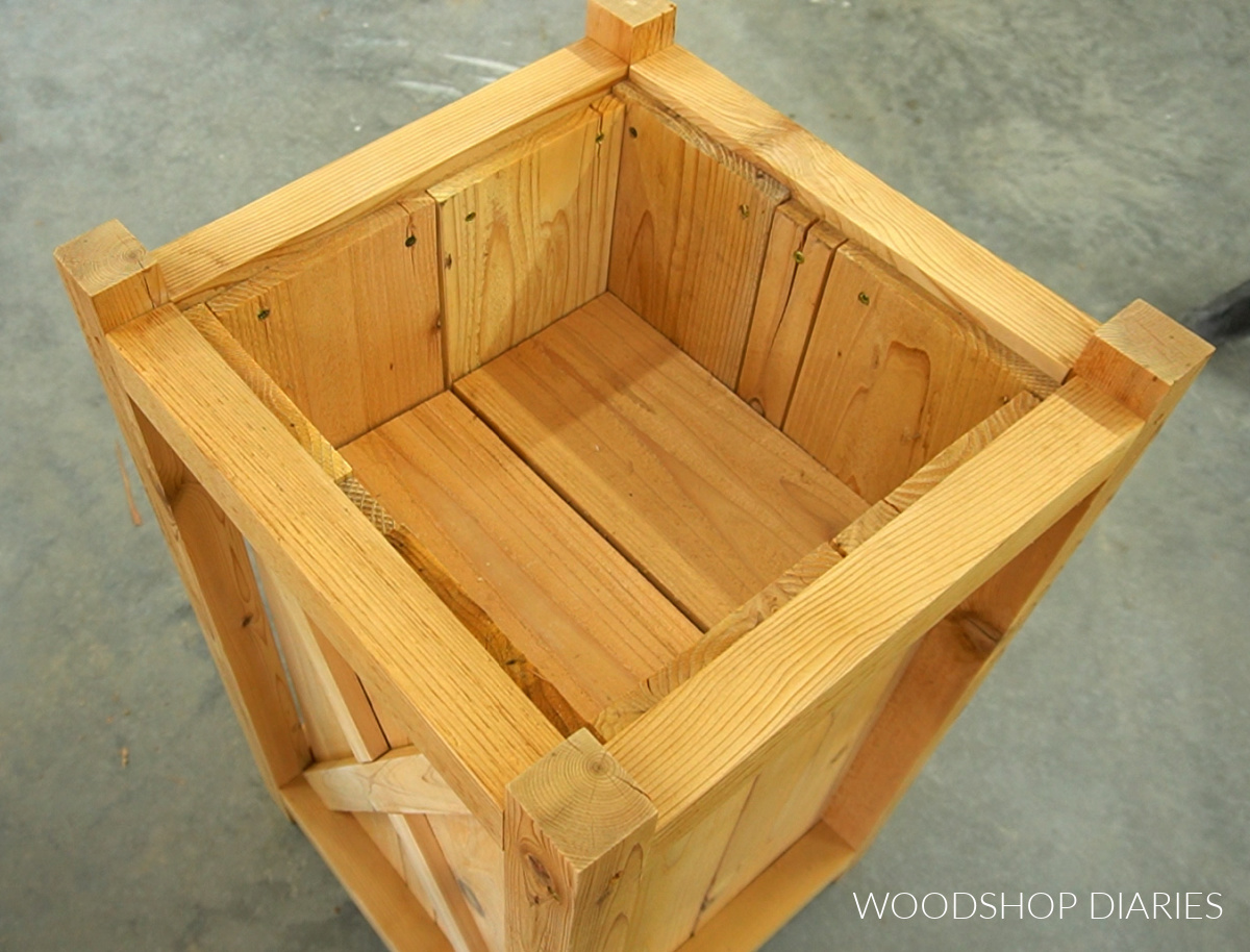 Shelf slats placed across shelf supports in wooden planter to rest plants on