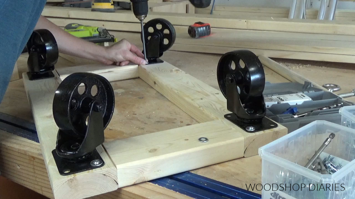 Screwing industrial casters onto bottom frame of wagon on workbench